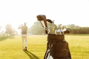 Photo of a bag of golf clubs with a man playing golf in the background
