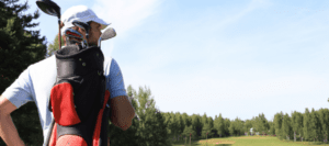 Man carrying bag of golf clubs across a golf course