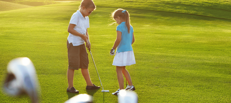 Two young kids (a boy and a girl) playing golf.